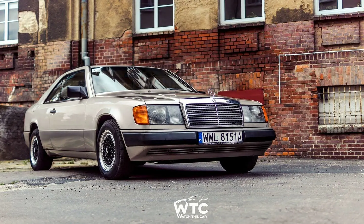 Prywatny Mercedes-Benz C124 właściciela CWR sfotografowany od przodu przed ceglanym budynkiem.